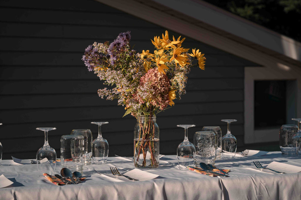 A dinner table set with glasses and a bouquet of wildflowers